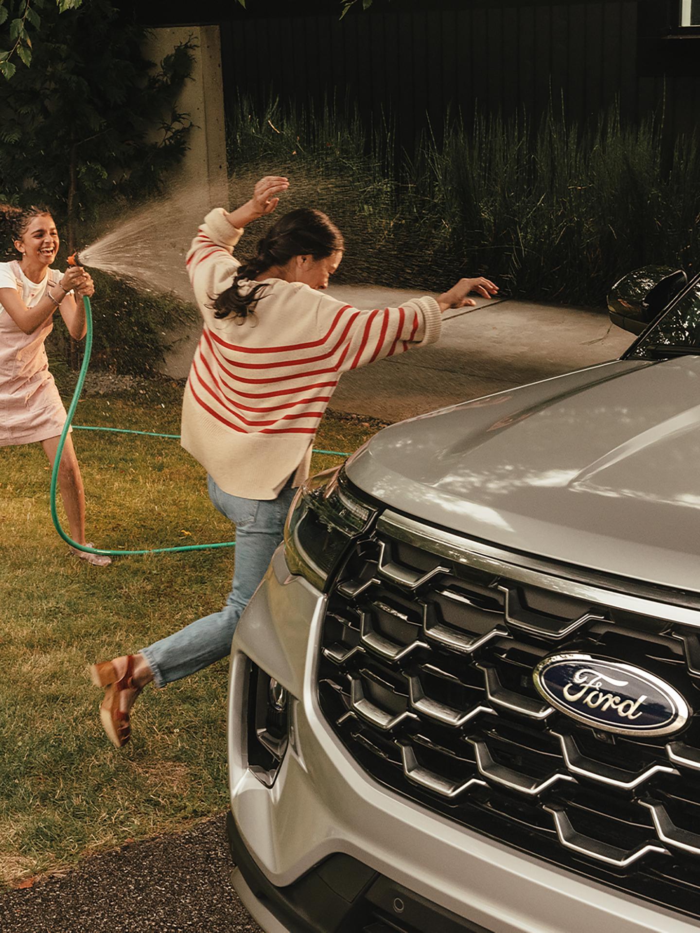 Une personne arrosant une autre personne avec un tuyau d’arrosage près d’un véhicule Ford.